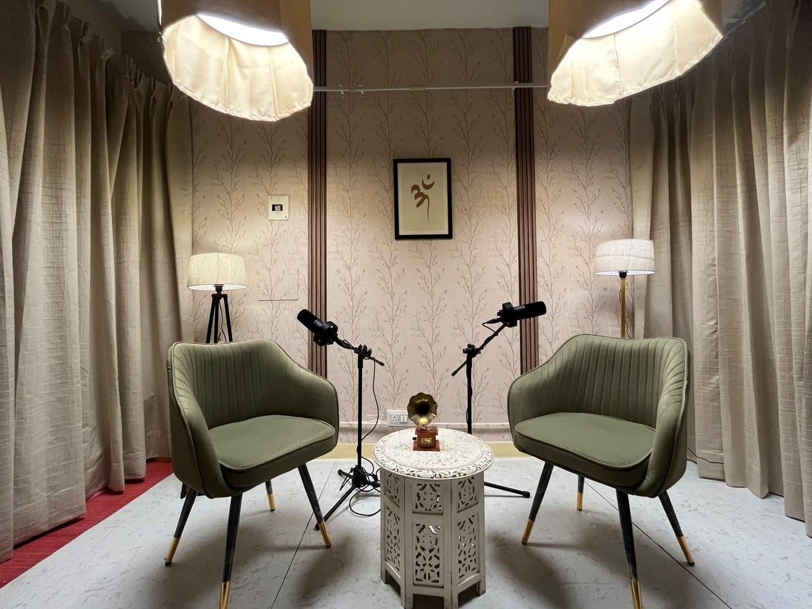 Wide view of the Dwarka podcast studio with two olive chairs, microphones, lighting and a round table